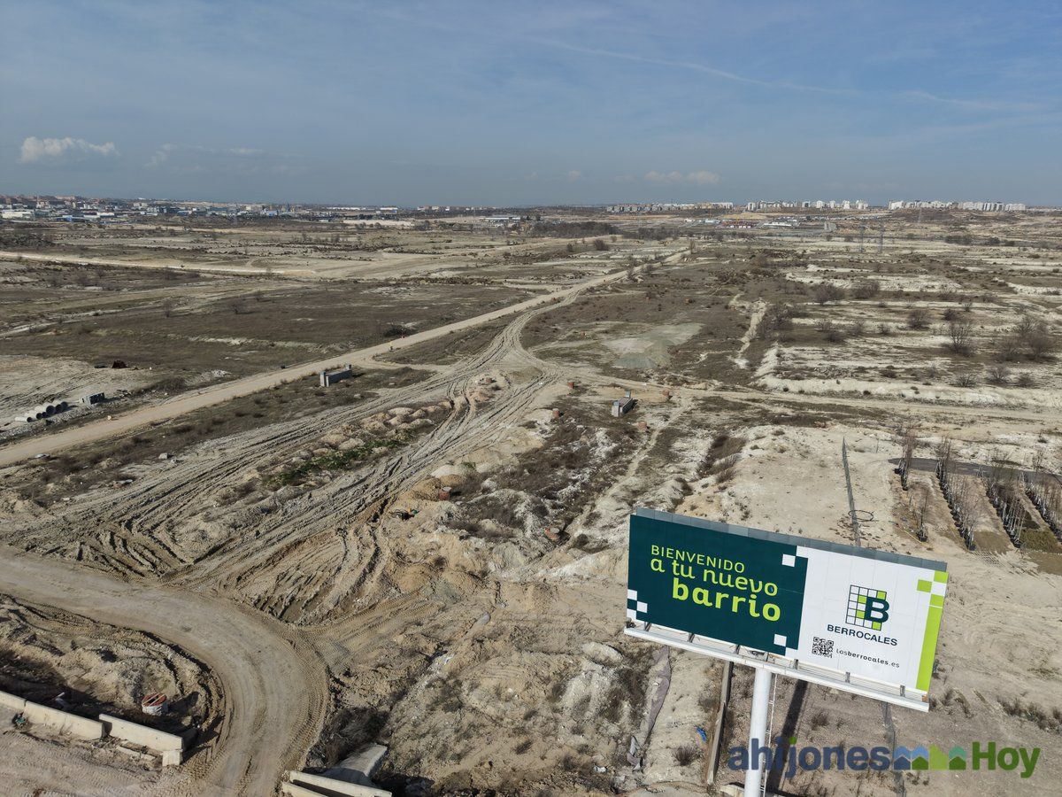 Cartel de bienvenida a Los Berrocales con las obras de urbanización al fondo